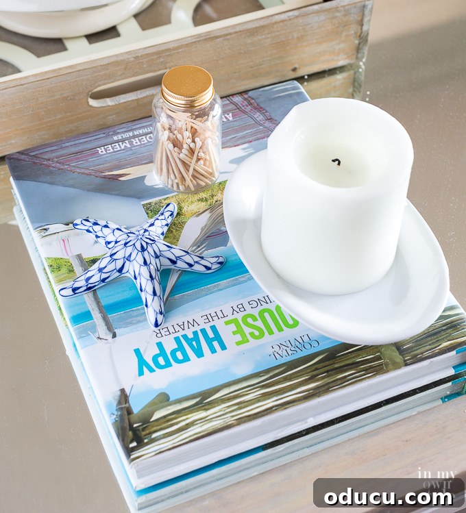 Instant Summer Room Makeover 2 A vibrant book on a coffee table, accompanied by a candle, ceramic starfish, and a glass bottle of matches, creating a charming summer decor vignette.
