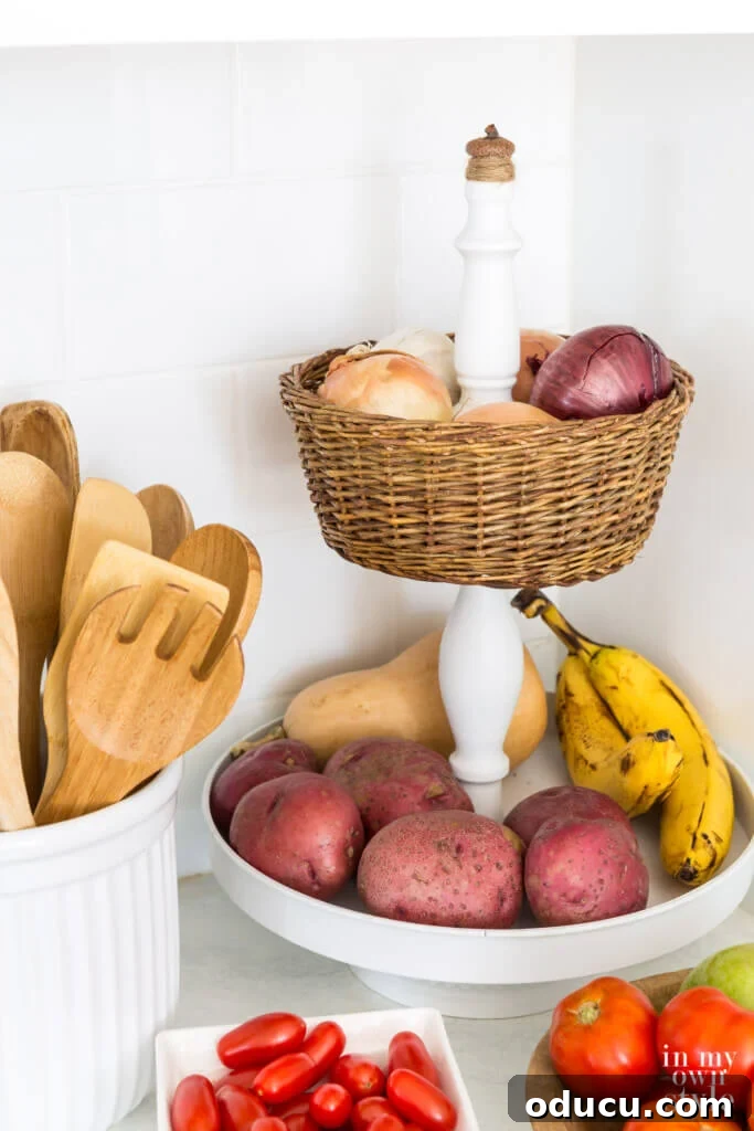 Crafting a Dual-Level Kitchen Storage Stand 14 DIY tiered kitchen fruit basket using a white metal stand and a thrift store basket. Another view of the DIY 2-tier fruit basket on a kitchen counter.