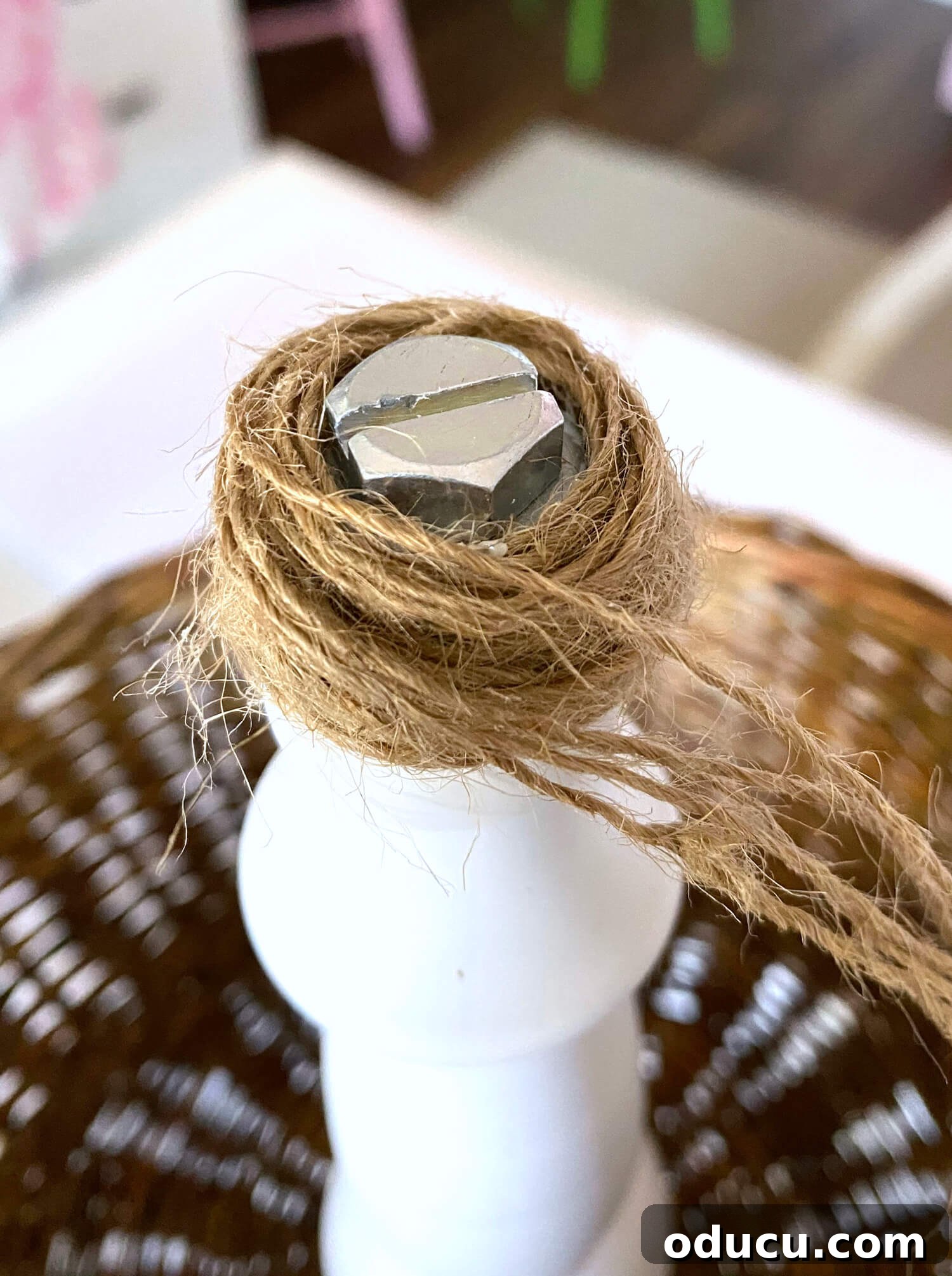 Crafting a Dual-Level Kitchen Storage Stand 9 Wrapping twine around screw and washer on the top of a tiered produce storage basket for a kitchen counter. Hands wrapping twine around the washers and screw to create a finial.