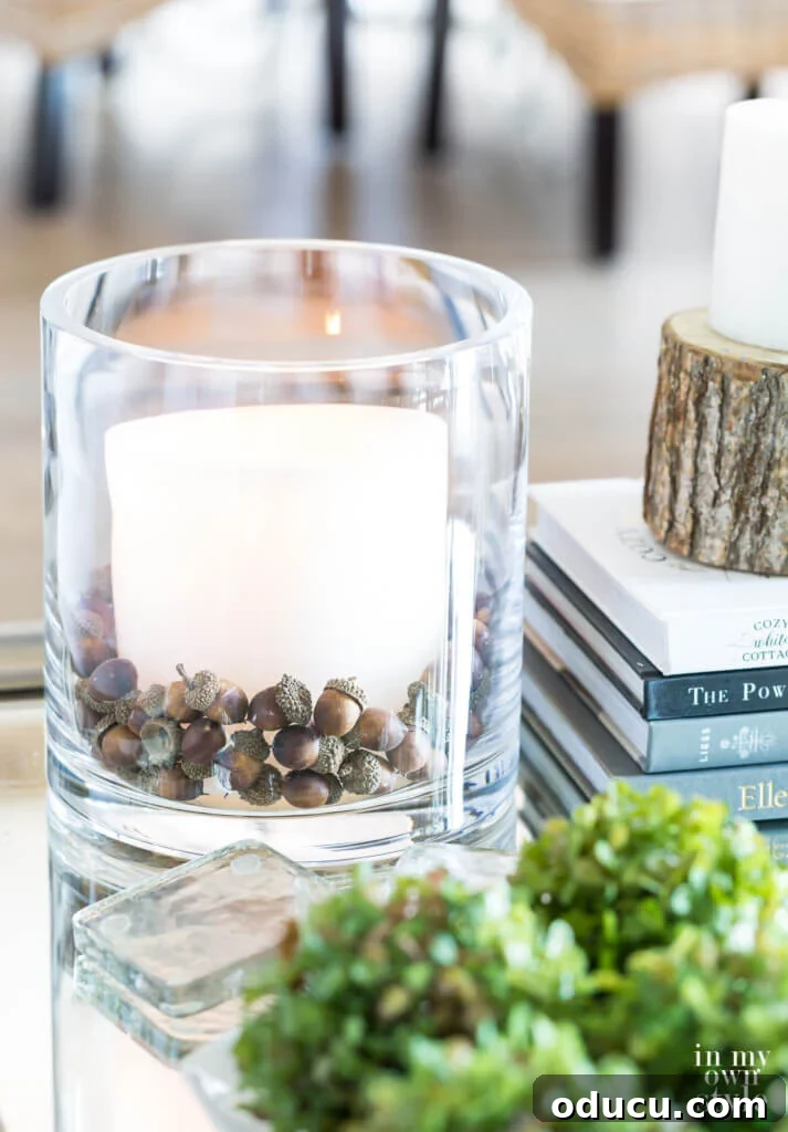 Autumn's Embrace: Natural Decor for Your Living Space 12 Pottery Barn glass cylinder vase filled with acorns and large white candle on a coffee table.