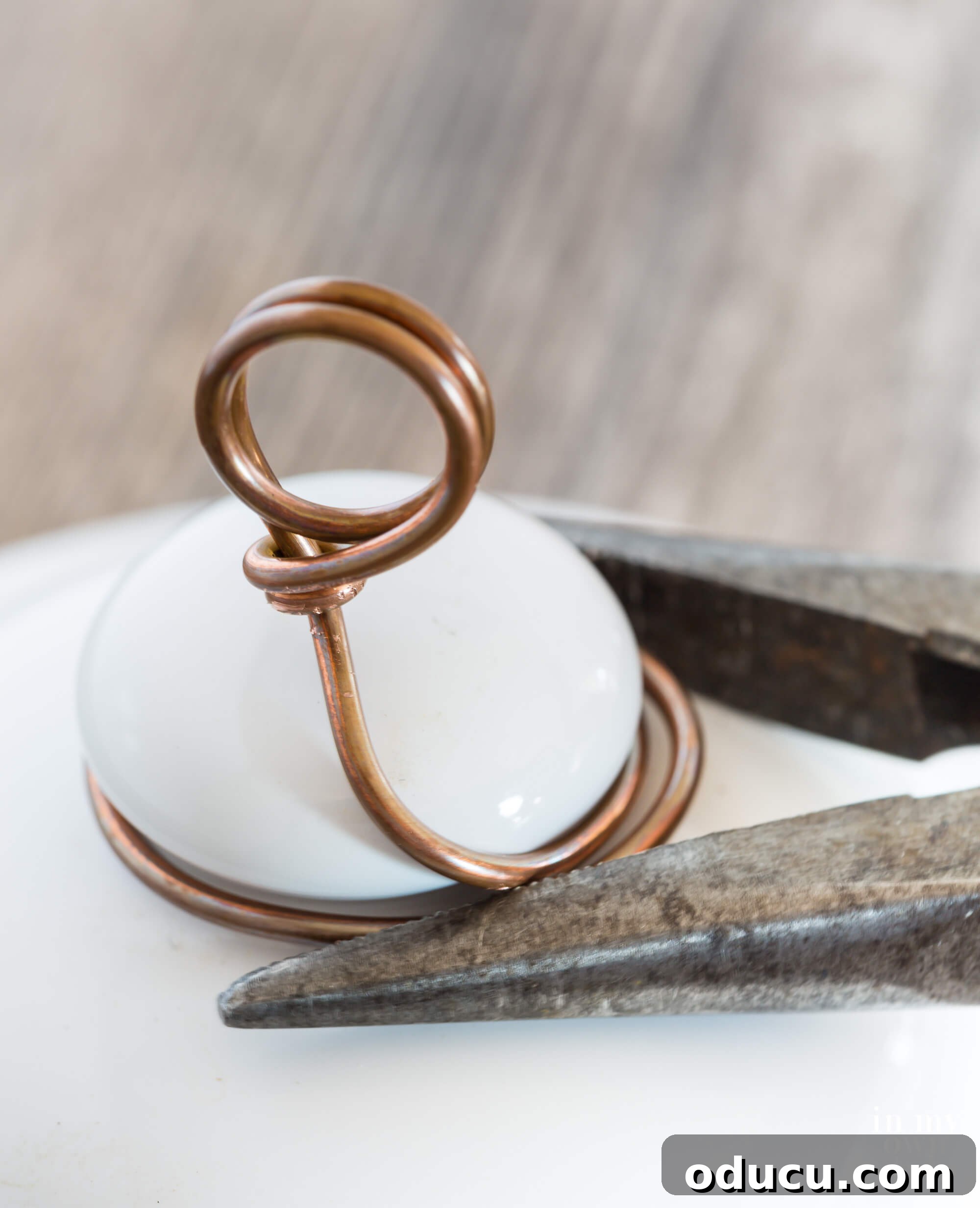Demonstration of using pliers to meticulously pull the wire tightly around the knob and trim any residual excess, achieving a clean and secure finish for the photo holder.