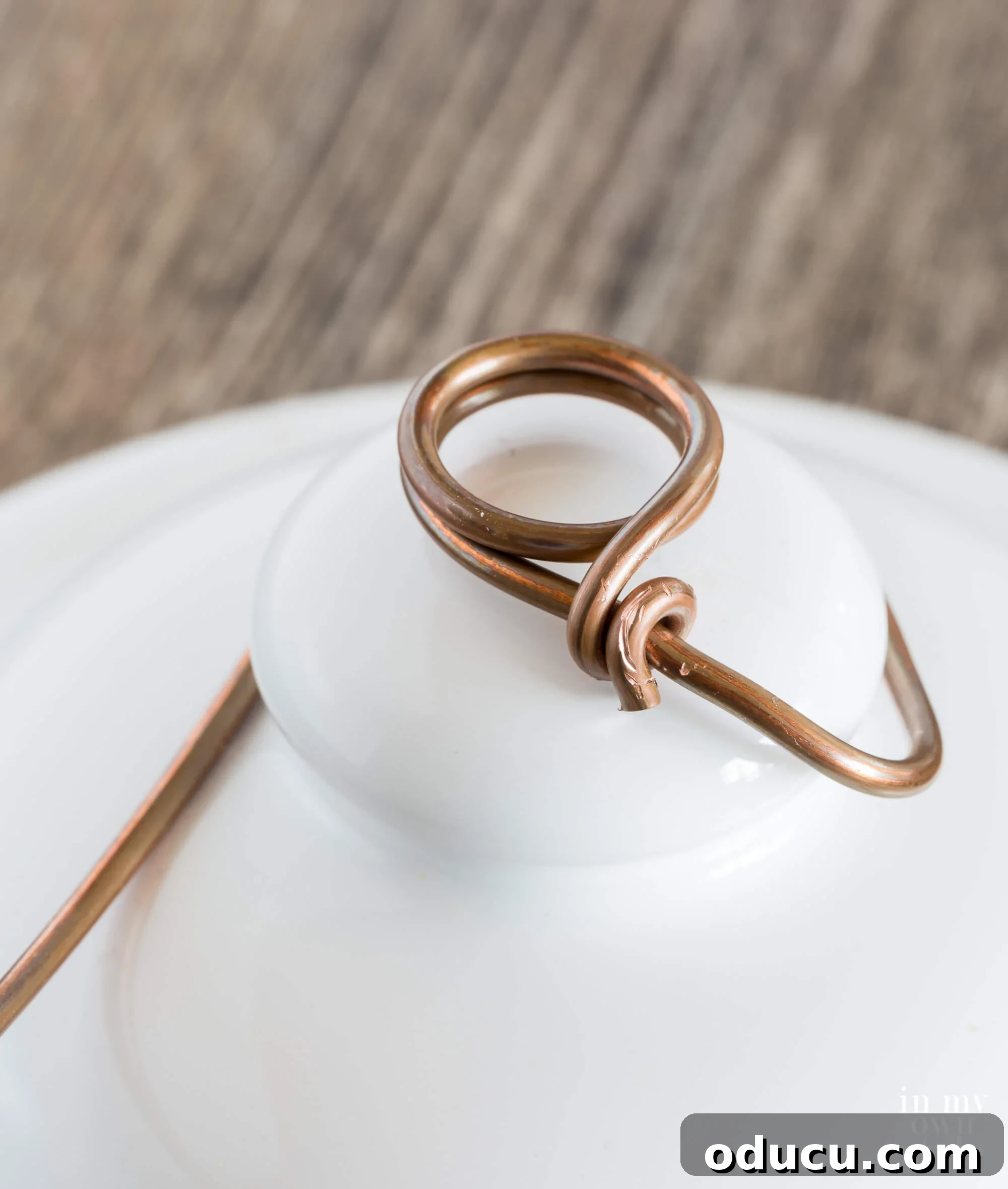 A visual guide demonstrating how to bend and firmly attach the wire to a ceramic jar top knob, initiating the photo holder assembly.