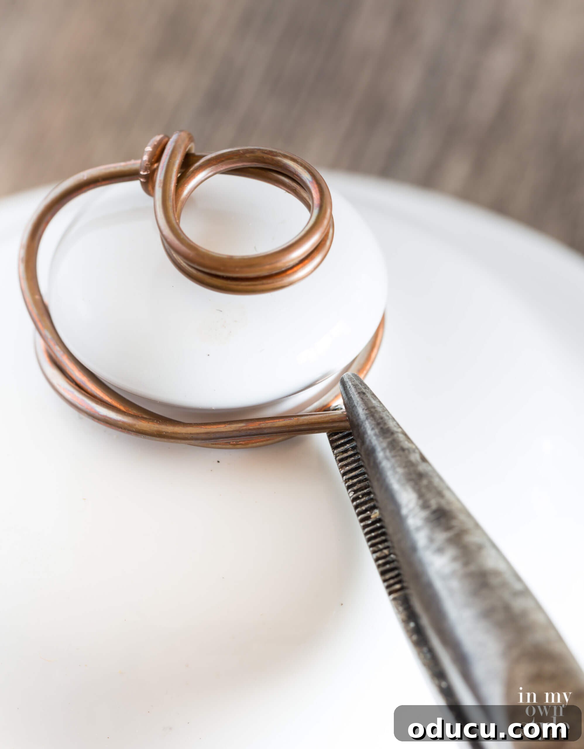 Detailed demonstration of how to firmly attach the wire around a ceramic jar top knob, creating a stable and aesthetic base for the photo holder.
