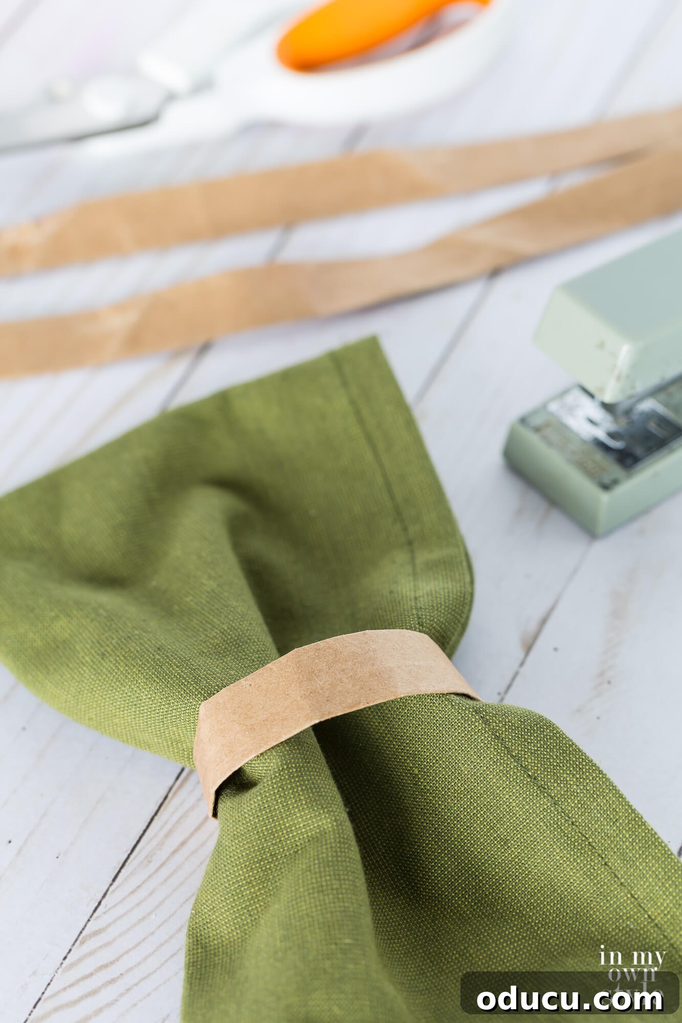 Thanksgiving Table Crafts: Free Placemats and Napkin Rings 14 Brown paper bag handle napkin ring on dark sage green napkin. Stapler and scissors in the background.