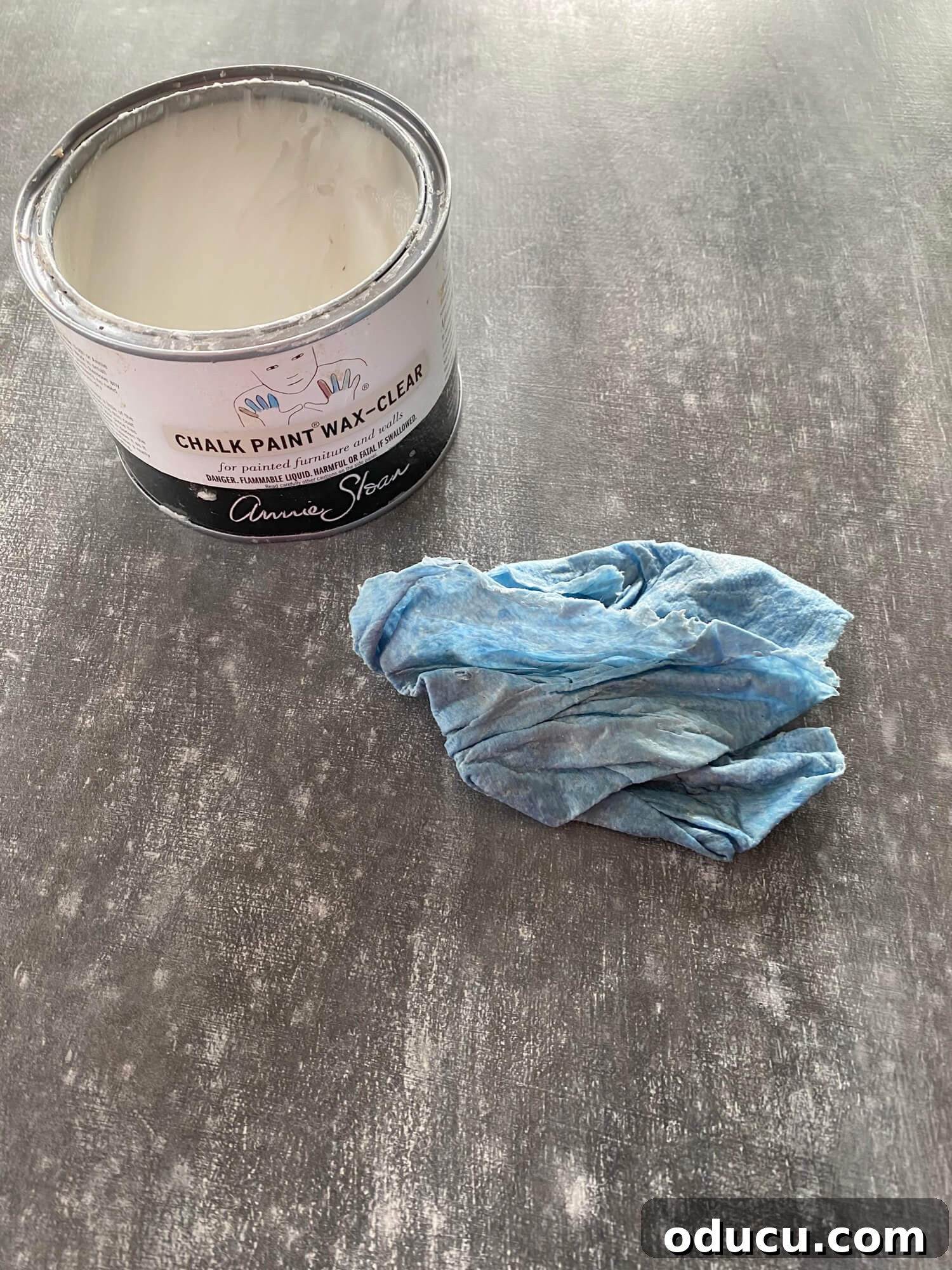 Annie Sloan clear wax being applied over a faux zinc painted table, demonstrating a crucial step in sealing and preparing the surface for further distressing and aging techniques. The wax provides a protective layer.