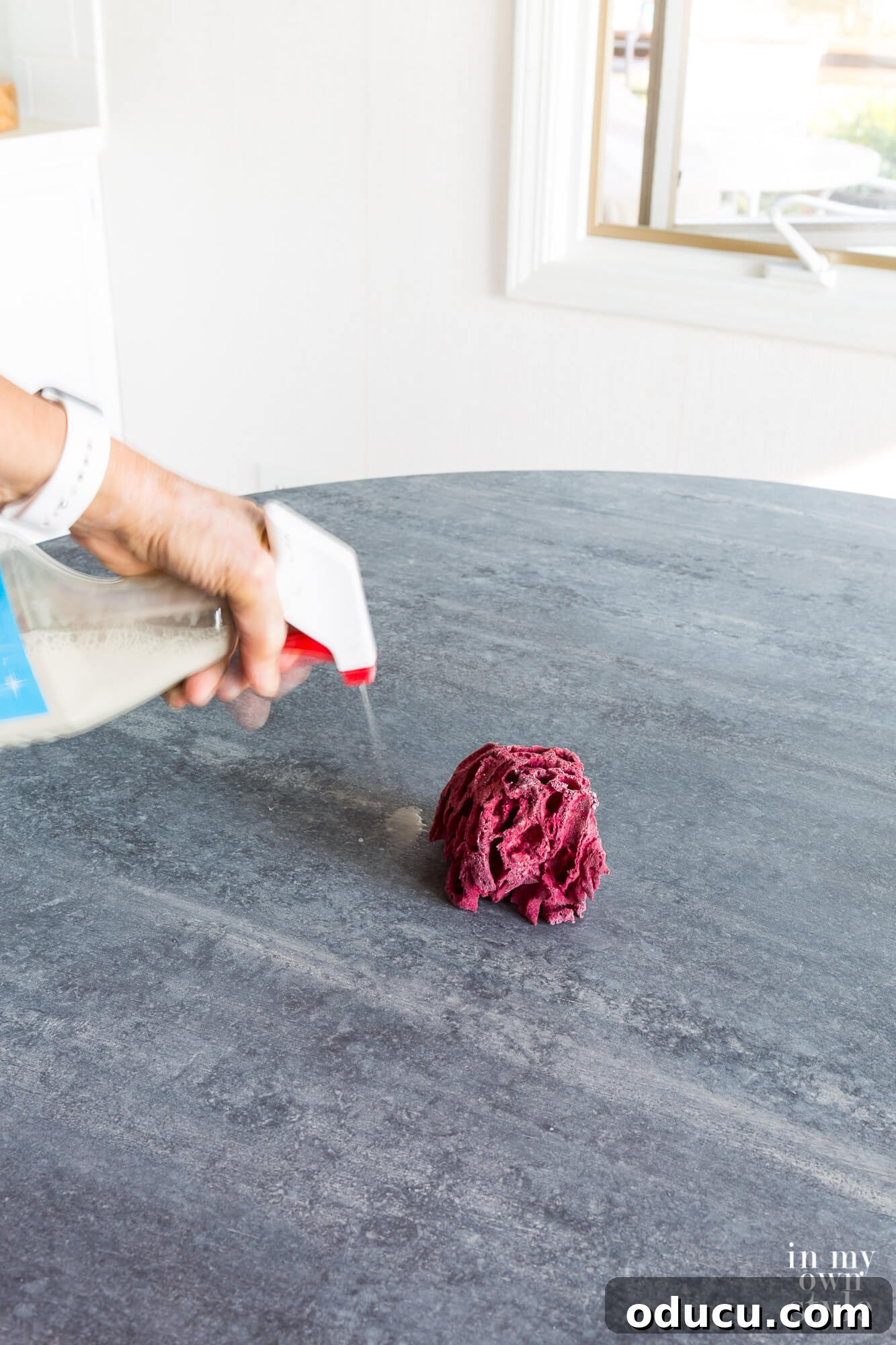 A person applying water over wet paint and sponging it off, demonstrating a technique to achieve blended and distressed effects for a faux zinc finish. This method allows for adjusting layers during the painting process.