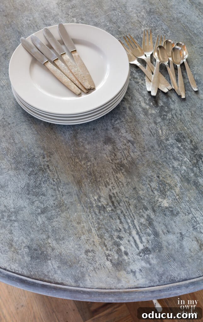 Zinc Effect Wooden Table Surfaces 22 A beautifully styled faux zinc painted table, featuring a stack of white plates and silverware, with a rustic fall floral arrangement at its center. This image showcases the elegance and versatility of the finished table in a home setting.