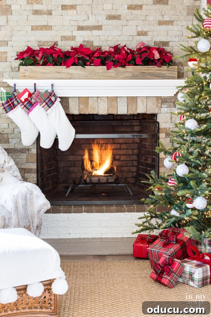 Effortless Festive Home Styling 13 A warm and inviting living room during Christmas, featuring a stone fireplace with a roaring fire, elegant white stockings hung, and a beautifully lit Christmas tree on the right.