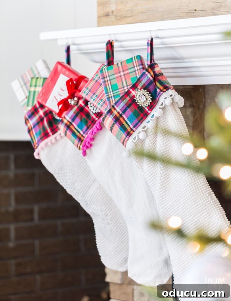 Effortless Festive Home Styling 14 Three elegant white Christmas stockings with festive plaid cuffs and playful pom-poms hang gracefully from a fireplace mantel, embodying a blend of rustic charm and holiday cheer.