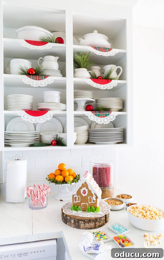 Effortless Festive Home Styling 21 Open white kitchen shelves are beautifully lined with red and plaid paper doilies, interspersed with red ornaments and natural pine sprigs, creating a charming and accessible Christmas display.
