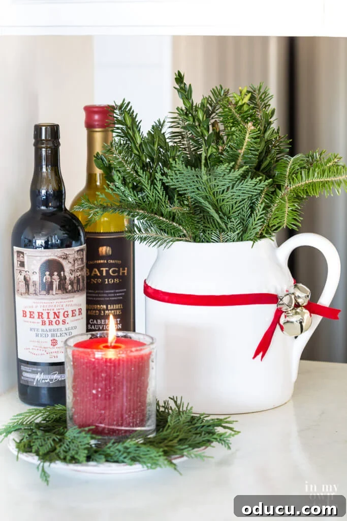Effortless Festive Home Styling 23 A charming kitchen counter vignette featuring wine bottles, a white pitcher filled with fresh pine, and jingle bells tied with a red ribbon, showcasing fast and easy Christmas decorating ideas.