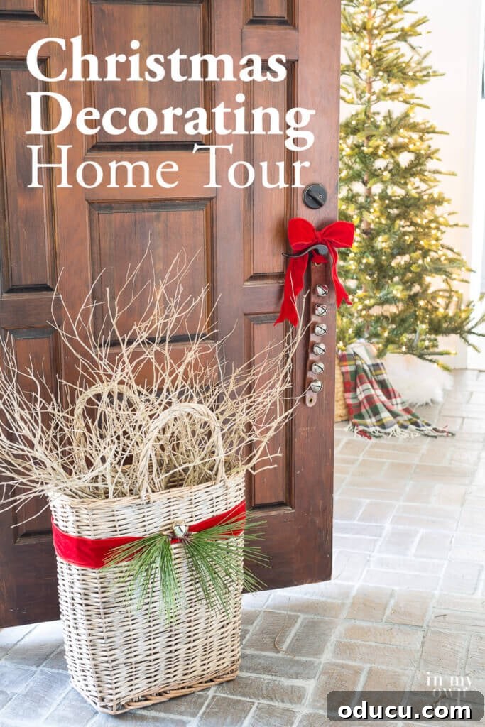 Effortless Festive Home Styling 29 A festive foyer with an open door revealing sleigh bells tied with red ribbon on the doorknob and a rustic basket, showcasing inviting Christmas decorating ideas for a home tour.