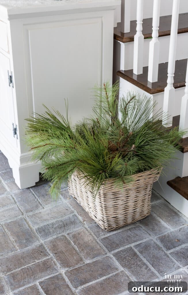 Effortless Festive Home Styling 6 A rustic woven basket, brimming with fresh evergreen branches, sits on the floor of a festive foyer, offering a simple yet impactful Christmas decorating idea.