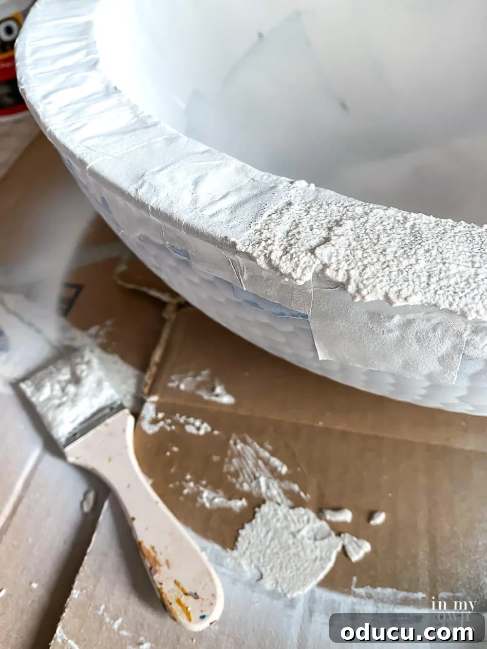 Spreading a thin layer of stucco patch onto the bowl's surface with a paint brush, creating the initial texture.