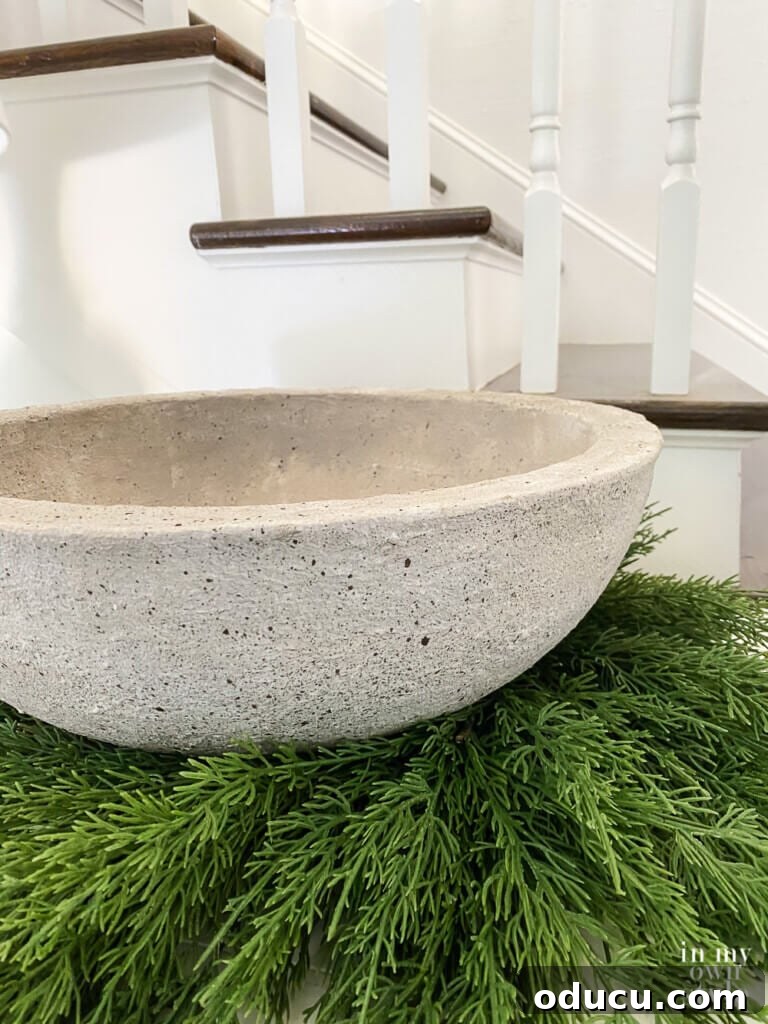 Close-up of the DIY faux concrete bowl planter, resting elegantly on a wreath on a sideboard, highlighting its realistic stone texture.