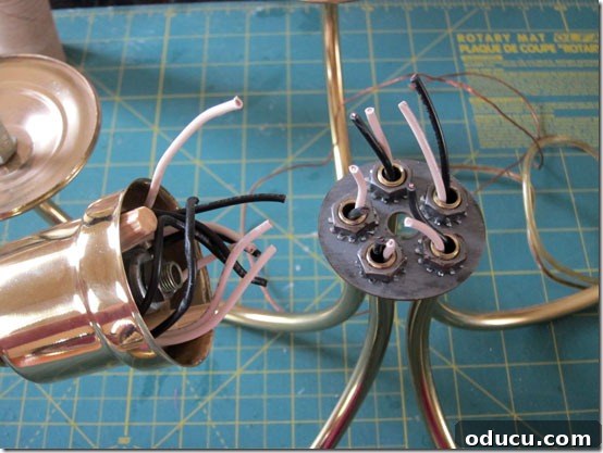 Sections of a brass chandelier disassembled for conversion into an outdoor lighting fixture, illustrating the removal of electrical components.