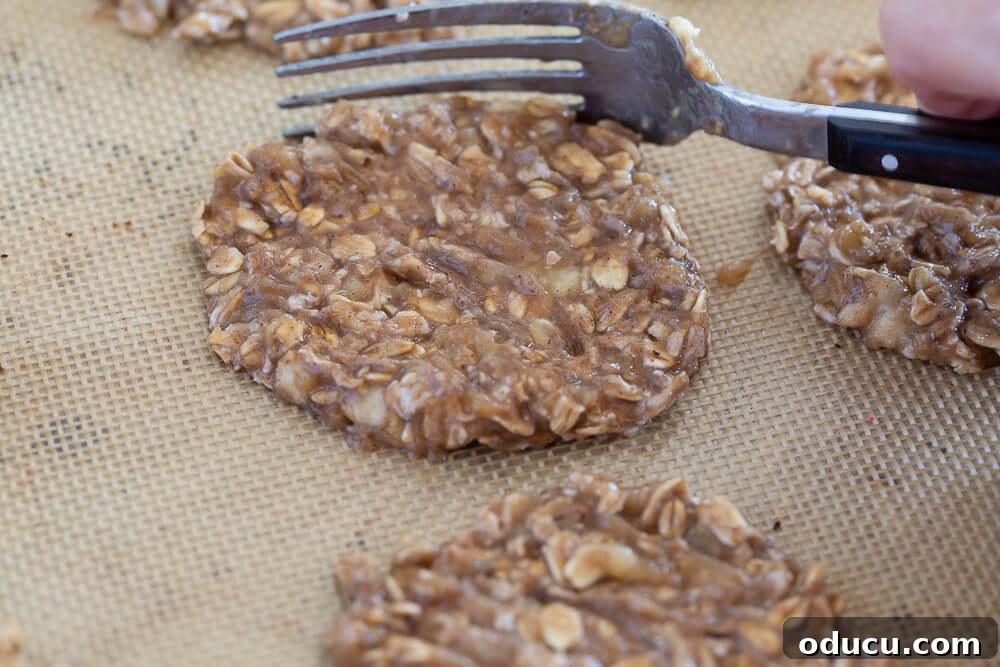 Wholesome Vegan Banana Oat Delights 11 Using a fork to meticulously flatten and shape a banana oatmeal cookie on a baking sheet, demonstrating precision.