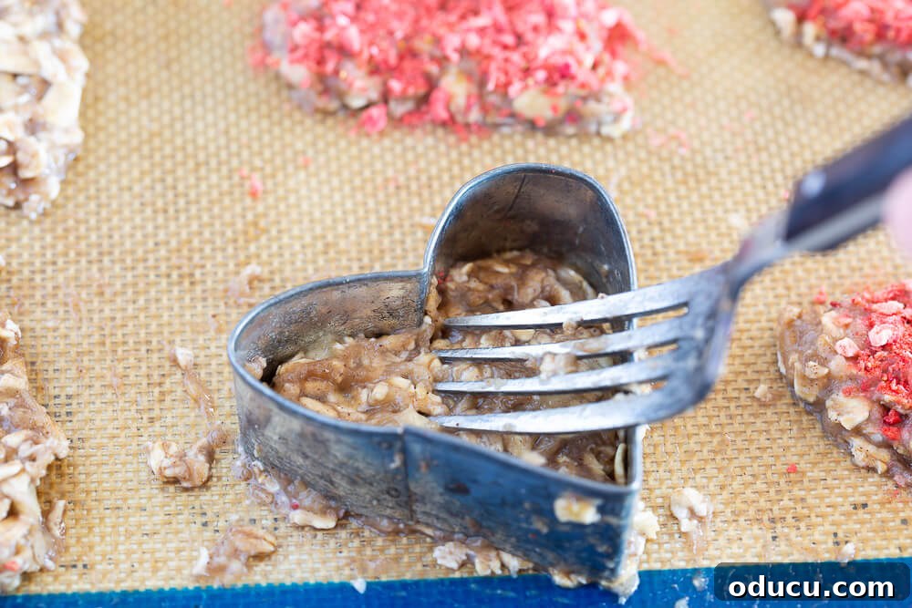Wholesome Vegan Banana Oat Delights 12 Banana oatmeal cookie batter being carefully pressed into a heart-shaped cookie cutter on a baking sheet using a fork.