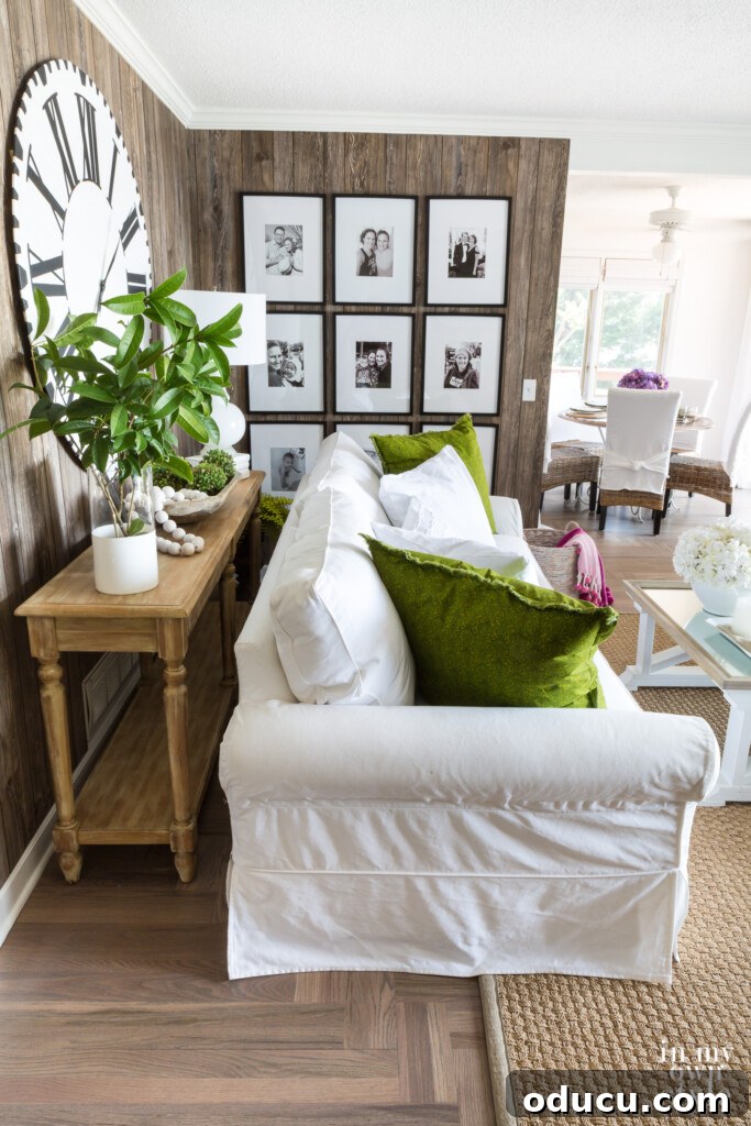 The Evolution of My Living Room Style 17 Faux barnwood paneled wall in living room with photo gallery, white sofa with green pillows and seagrass rug.