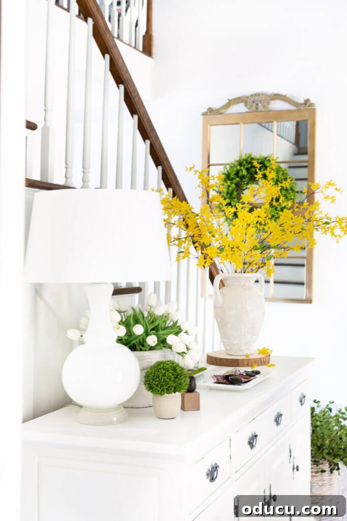 Blossom Your Entryway This Spring 5 Forsythia and white tulips arranged on a long white dresser in an entryway foyer decorated for spring.