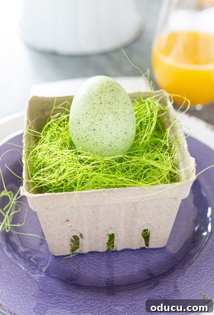 Cardboard berry crate filled with green Easter grass and a pale green speckled egg. Sitting on the center of a purple dinner plate.