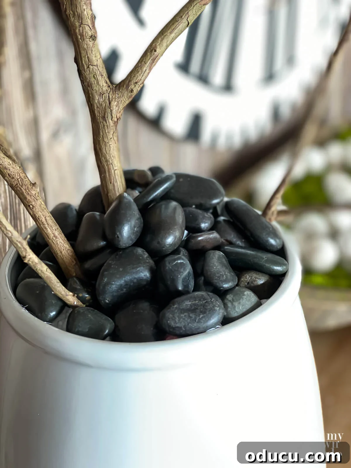 Black river rocks used instead of moss in a ceramic planter filled with Faux blooming branches.