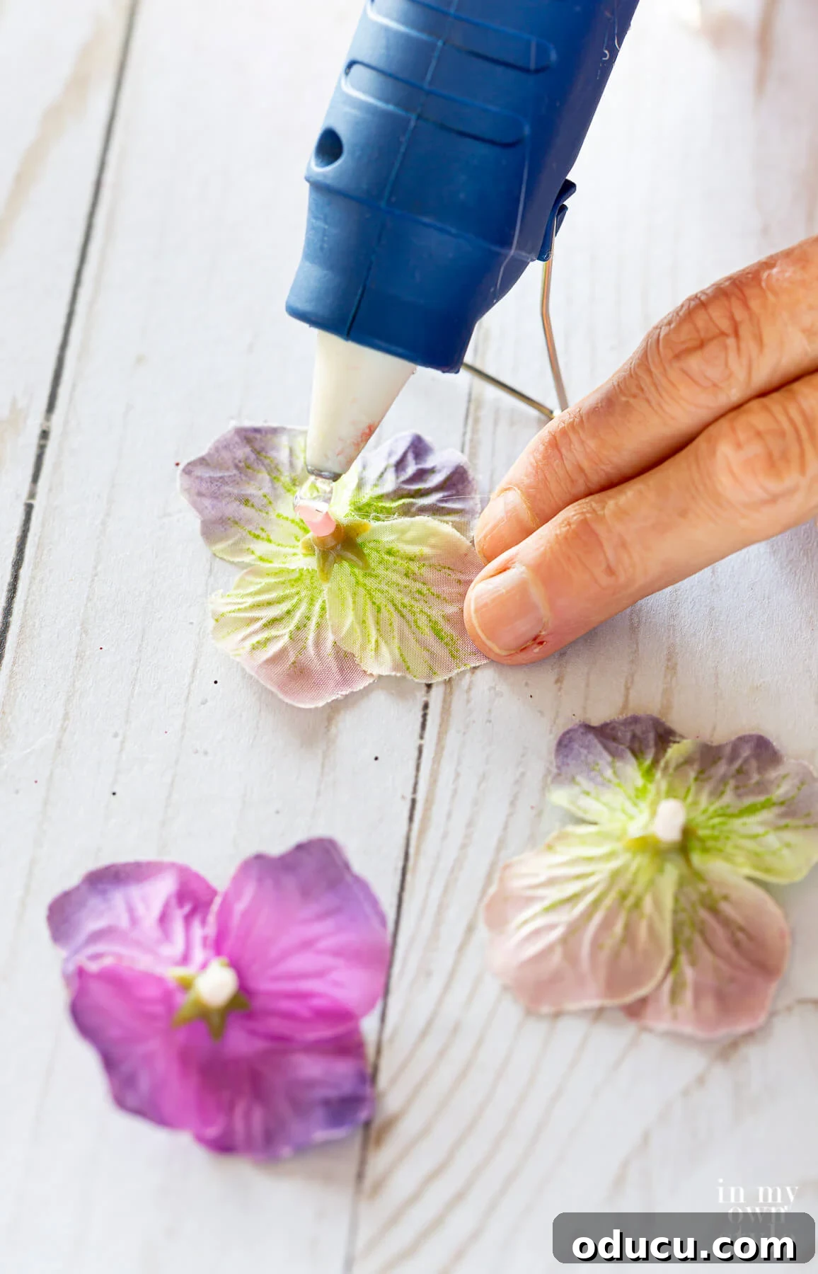 Adding hot glue to the back of snipped purple flower blooms from a fake flower stem.