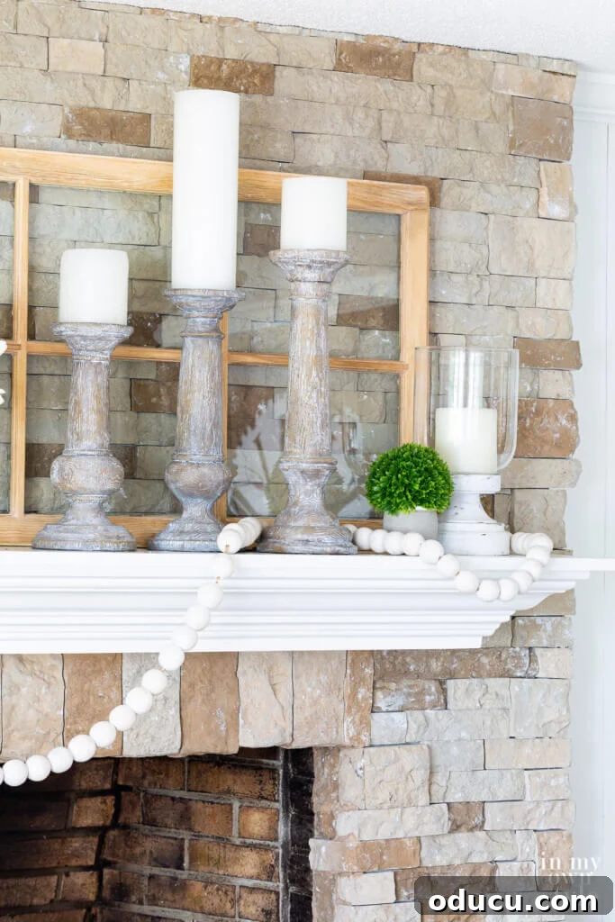 Close-up of three white-washed wood candle holders with white pillar candles, creating a serene focal point on a summer fireplace mantel.