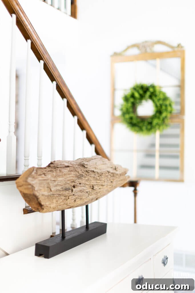 Modern art made using driftwood and parts of a wood pallet in a home foyer, with a large DIY mirror in the background.