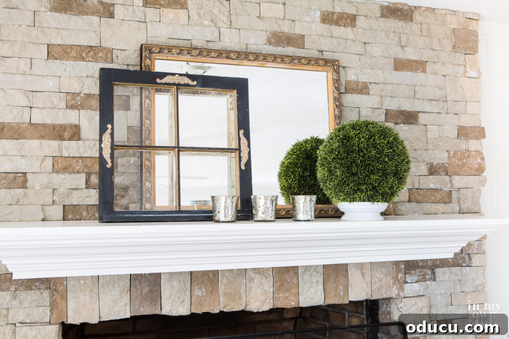 A mantel styled for winter using a small wood window frame, elegantly painted in black and gold as an accent piece.