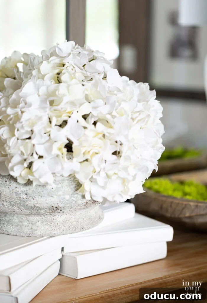 Grand Living Room on a Small Budget: $240 Makeover 11 Elegant white hydrangeas artfully arranged on a stack of white books, set against a stunning wall of mirrors.