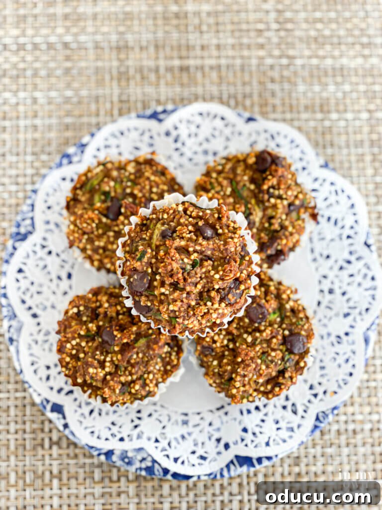 Vegan no-oil zucchini muffins stacked on a doily covered blue and white plate. This whole-food, plant-based zucchini muffin recipe has a surprise ingredient. It is what makes the muffins taste so good. Moist with a little bit of crunch. The recipe can easily be made in a loaf pan and freezes well.