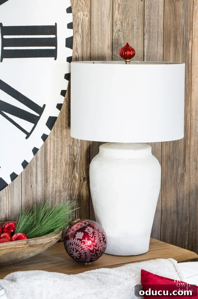 Craft Stunning Table Lamps for Less 15 Holiday lamp finial idea. Close up of white table lamp with red Christmas ball ornament made into a finial above the lamp shade.