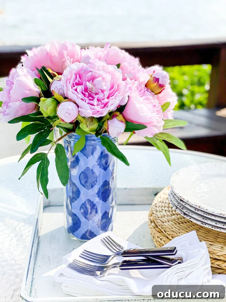 Deck Decor Hacks That Won't Empty Your Wallet 18 Pink peonies in a tall glass vase with two-tone blue pattern gift wrap wrapped around it.