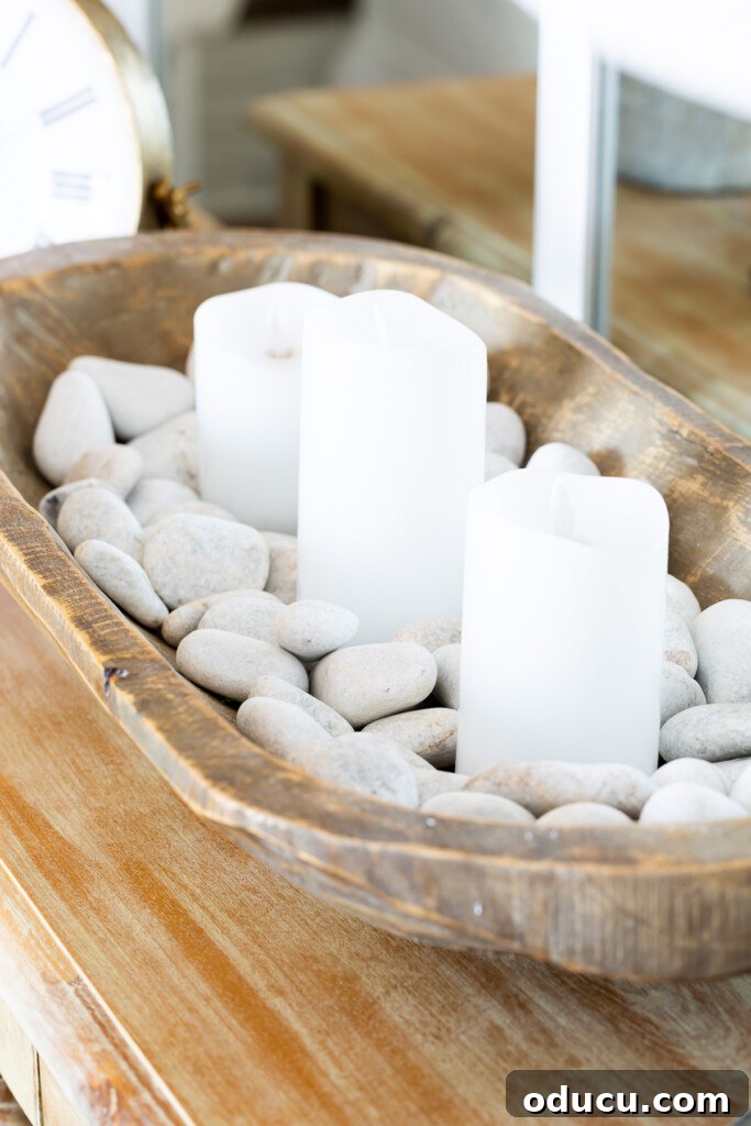 12 Affordable DIY Summer Decor Projects 18 A rustic dough bowl filled with smooth white river rocks and flickering white candles, creating a serene focal point for a living room table.