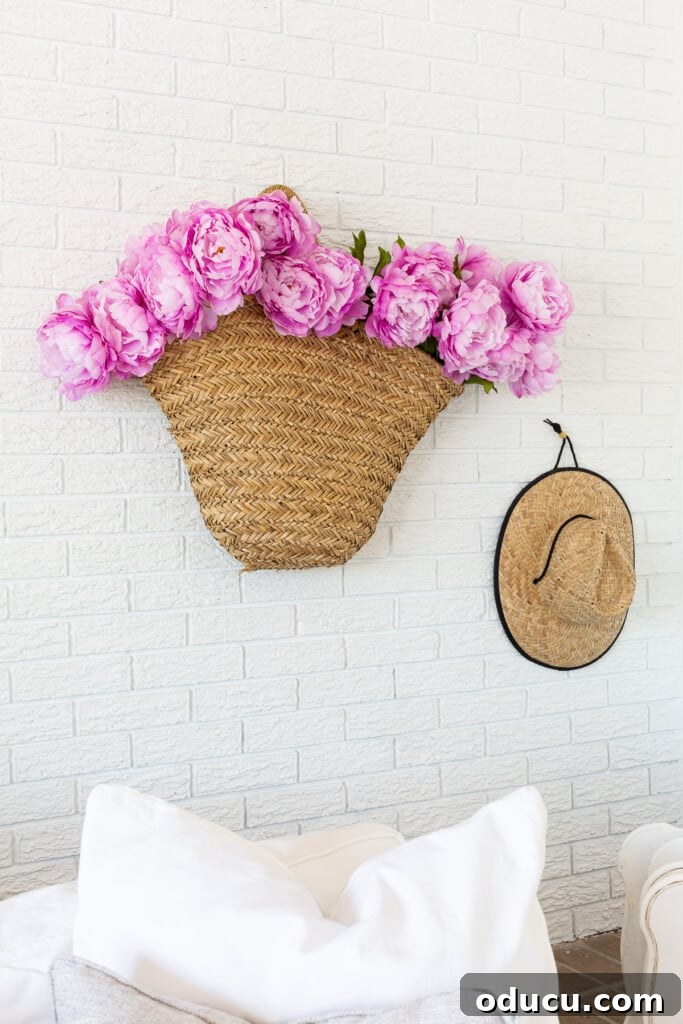 12 Affordable DIY Summer Decor Projects 3 A woven basket tote filled with vibrant pink peonies hanging gracefully on a living room wall, offering a unique floral display.