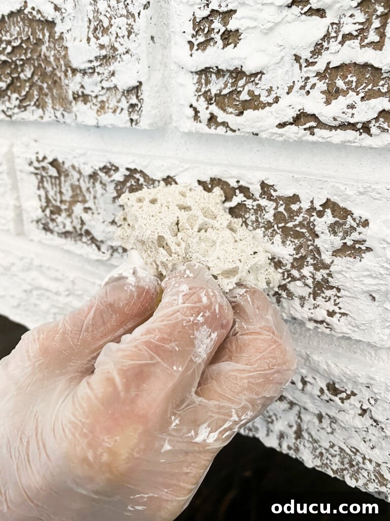 12 Affordable DIY Summer Decor Projects 6 A close-up view of the diligent process of painting a brick fireplace wall white in a living room, highlighting the attention to detail.