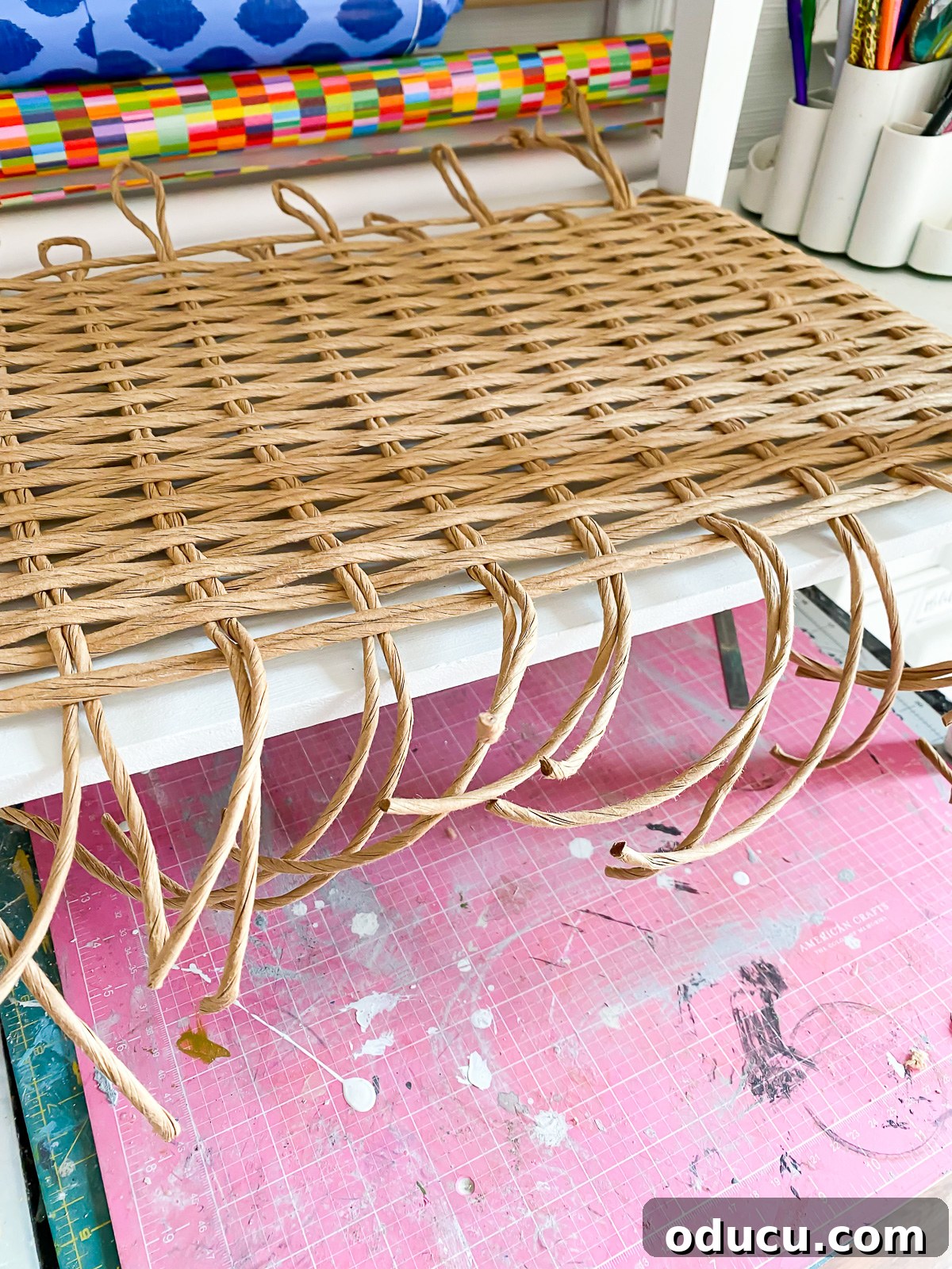 Designer Dupe Two-Tier End Table Makeover 24 Image showing rattan fiber rush woven on a table where the ends are pulled to the underside but not yet secured.