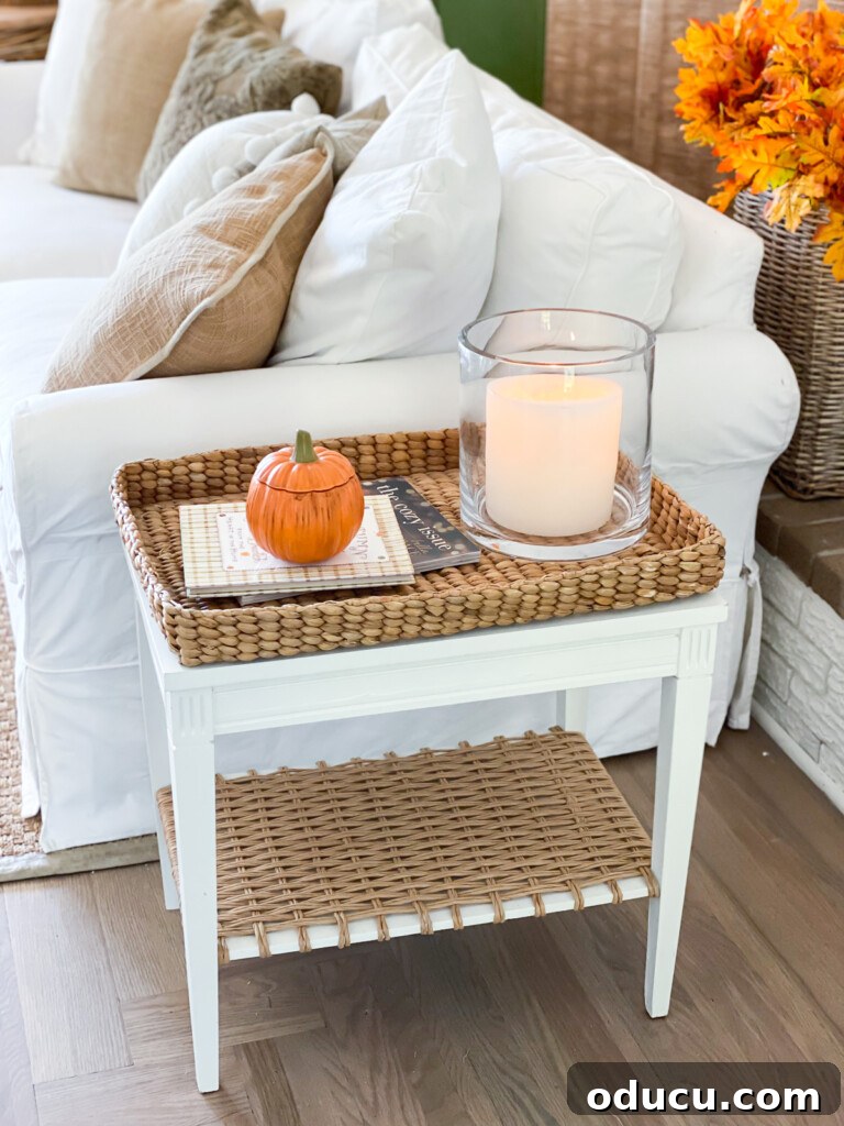 Embracing Autumn Hues in Your Living Space 9 Two-tier white side table with a woven tray, a small ceramic pumpkin, and a candle in a glass hurricane, showcasing meaningful fall decor.