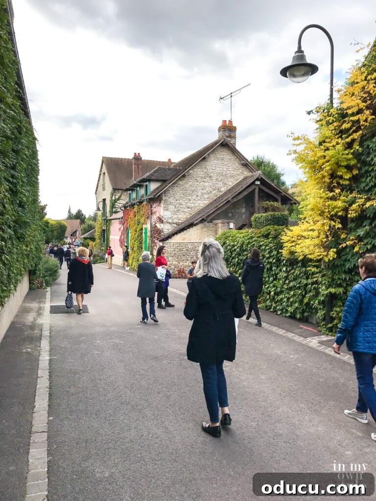 Tourists enjoying a leisurely walk along a picturesque road in Giverny, France, surrounded by natural beauty.