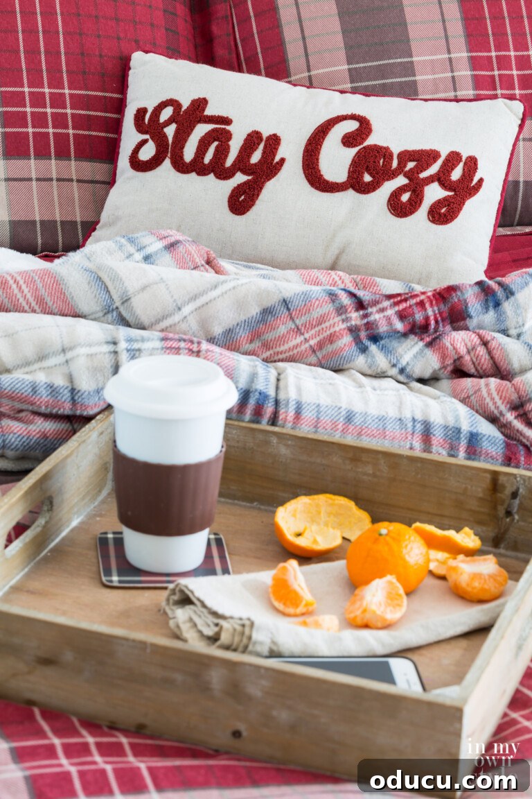 A 'Stay Cozy' pillow resting on a well-made guest room bed, featuring plaid CuddlDuds bedding, inviting comfort and warmth.