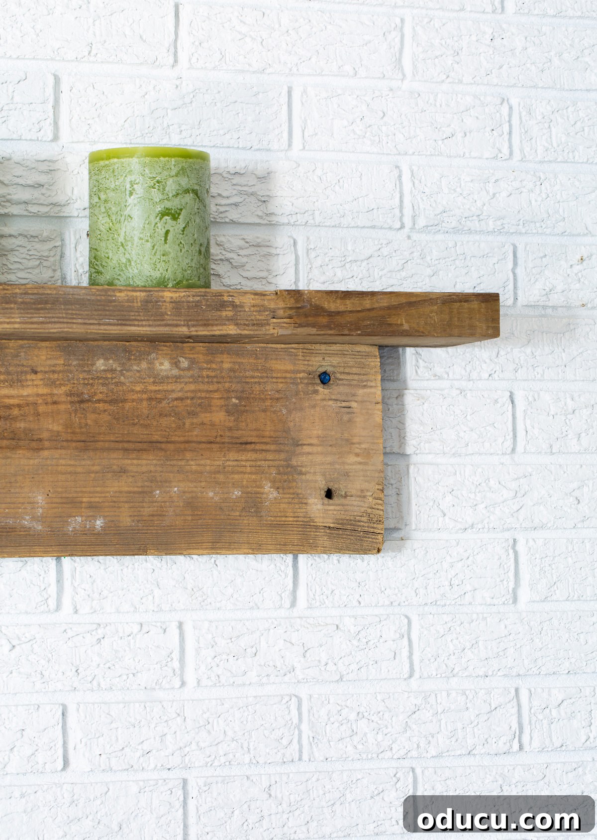 Close up of end of rustic reclaimed wood mantel on white brick wall.