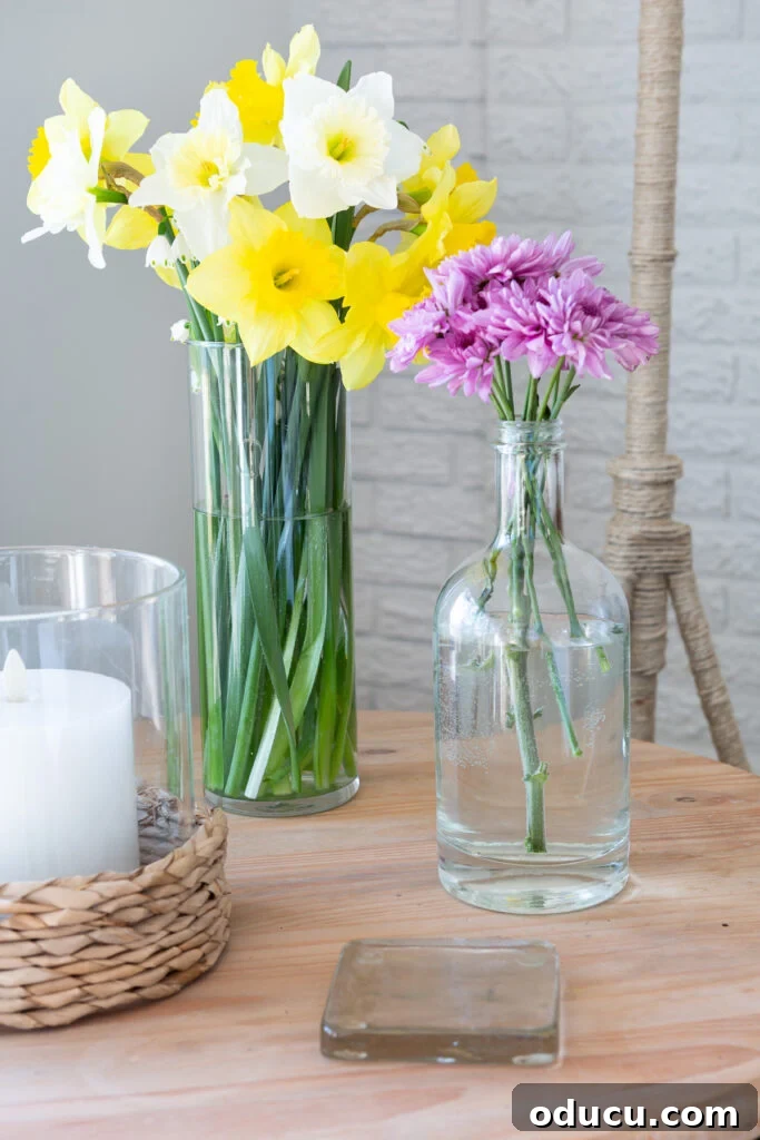 Repurpose Your Jewelry for Home Decor 2 A glass vase and an upcycled bottle, both holding spring flowers, with necklaces wrapped around them.