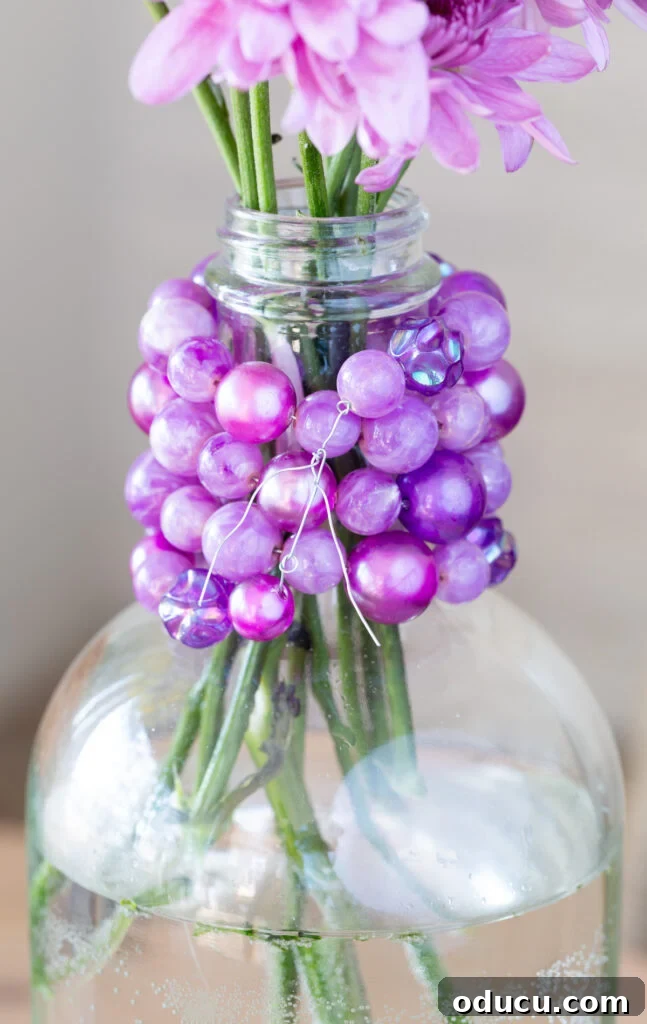 Repurpose Your Jewelry for Home Decor 5 Detailed view of how to use florist wire to attach an old costume jewelry necklace around a glass bottle to create a beautiful vase.