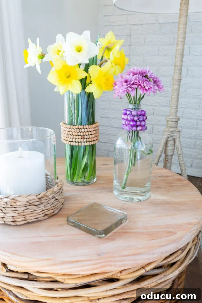 Repurpose Your Jewelry for Home Decor 6 A beautifully decorated glass vase and bottle, wrapped with old jewelry necklaces, bringing colorful spring decor to a side table.