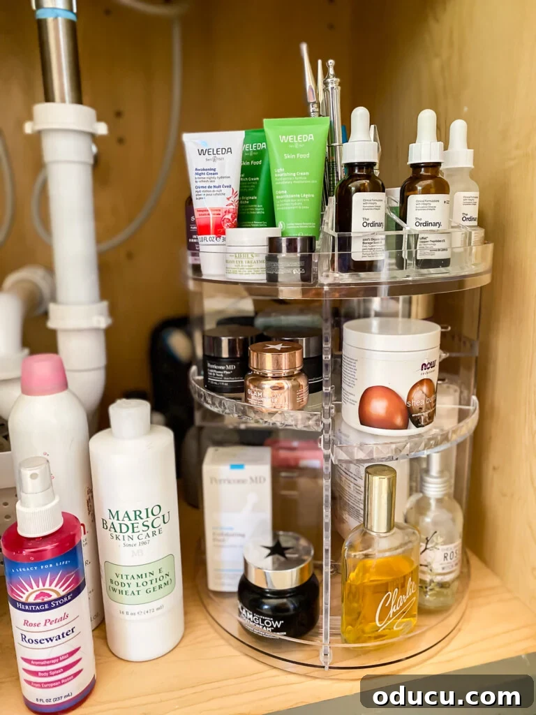 Triple-Tier Revolving Bathroom Organizer 5 Under a bathroom sink, a clear acrylic 3-tier rotating bathroom organizer holding various items.