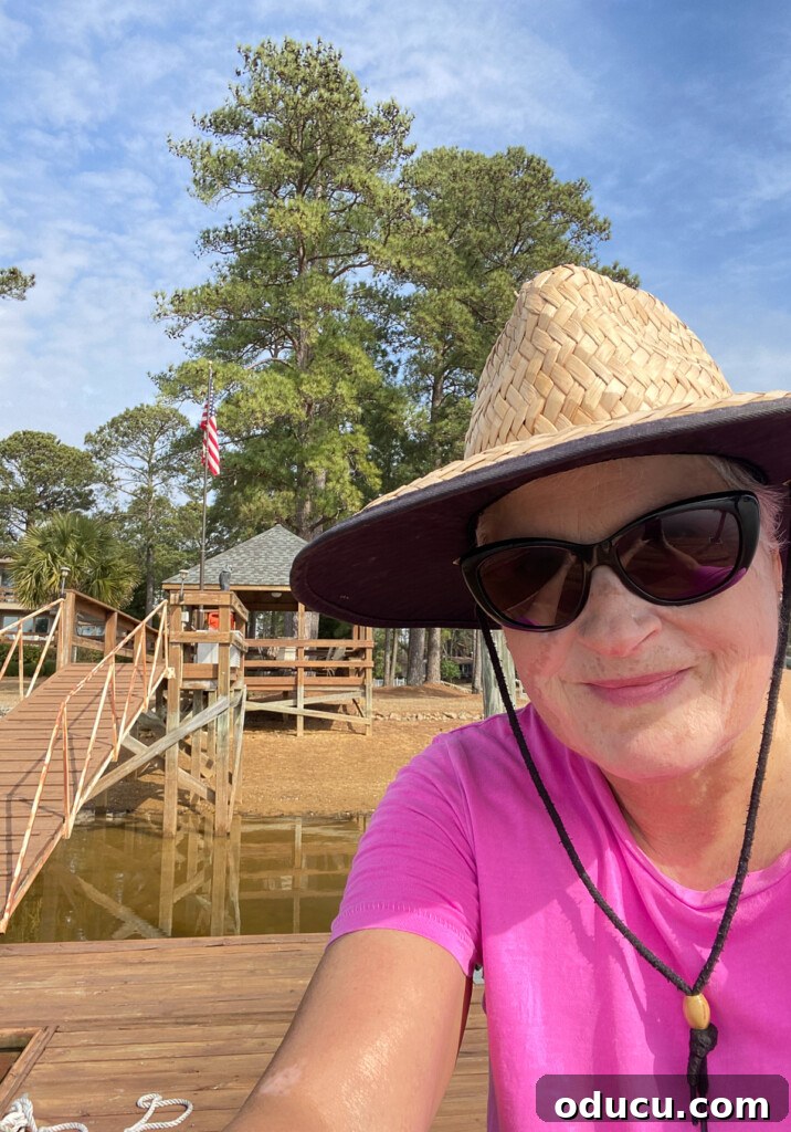 Our Teacup Talk 5 Blogger Diane, wearing a wide-brimmed hat, smiles on a dock by the lake, enjoying the outdoors.