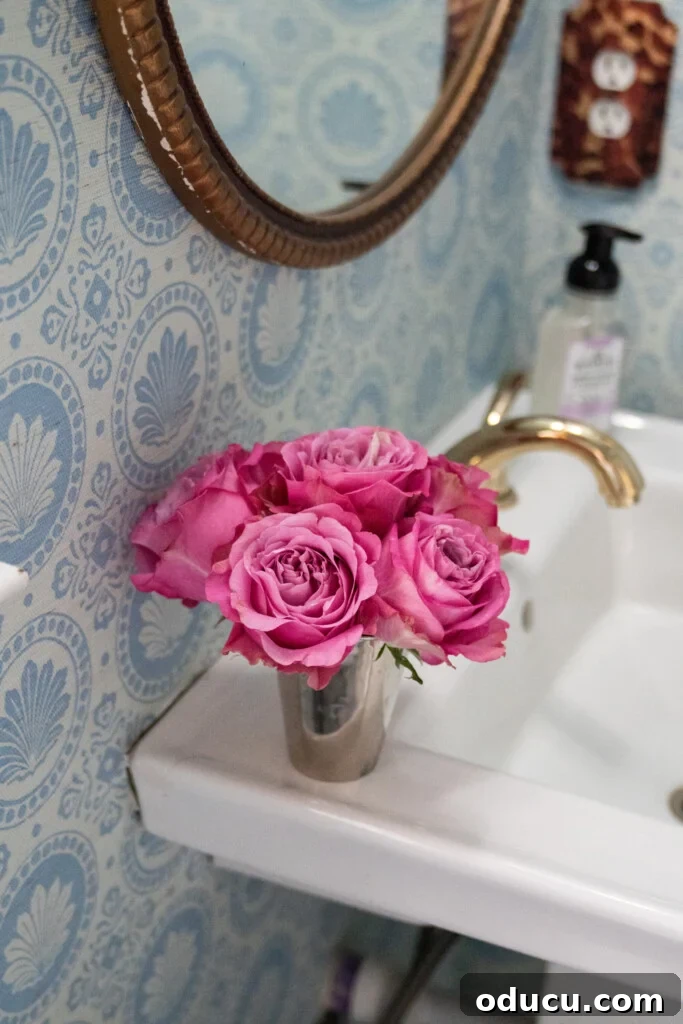 Trendspotting: Issue 130 2 A beautifully decorated powder room featuring elegant blue and white patterned wallpaper, a sleek dark vanity, and a chic round mirror, creating a high-impact design statement in a compact space.