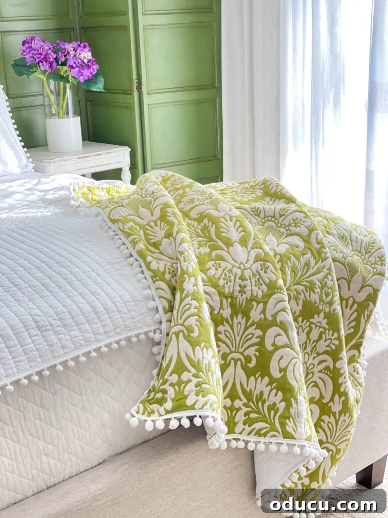 Revitalize Your Bedroom: Creative Decor Transformations 5 A green and white throw blanket draped elegantly over the foot of a bed adorned with crisp white bedding, creating a fresh and inviting atmosphere.