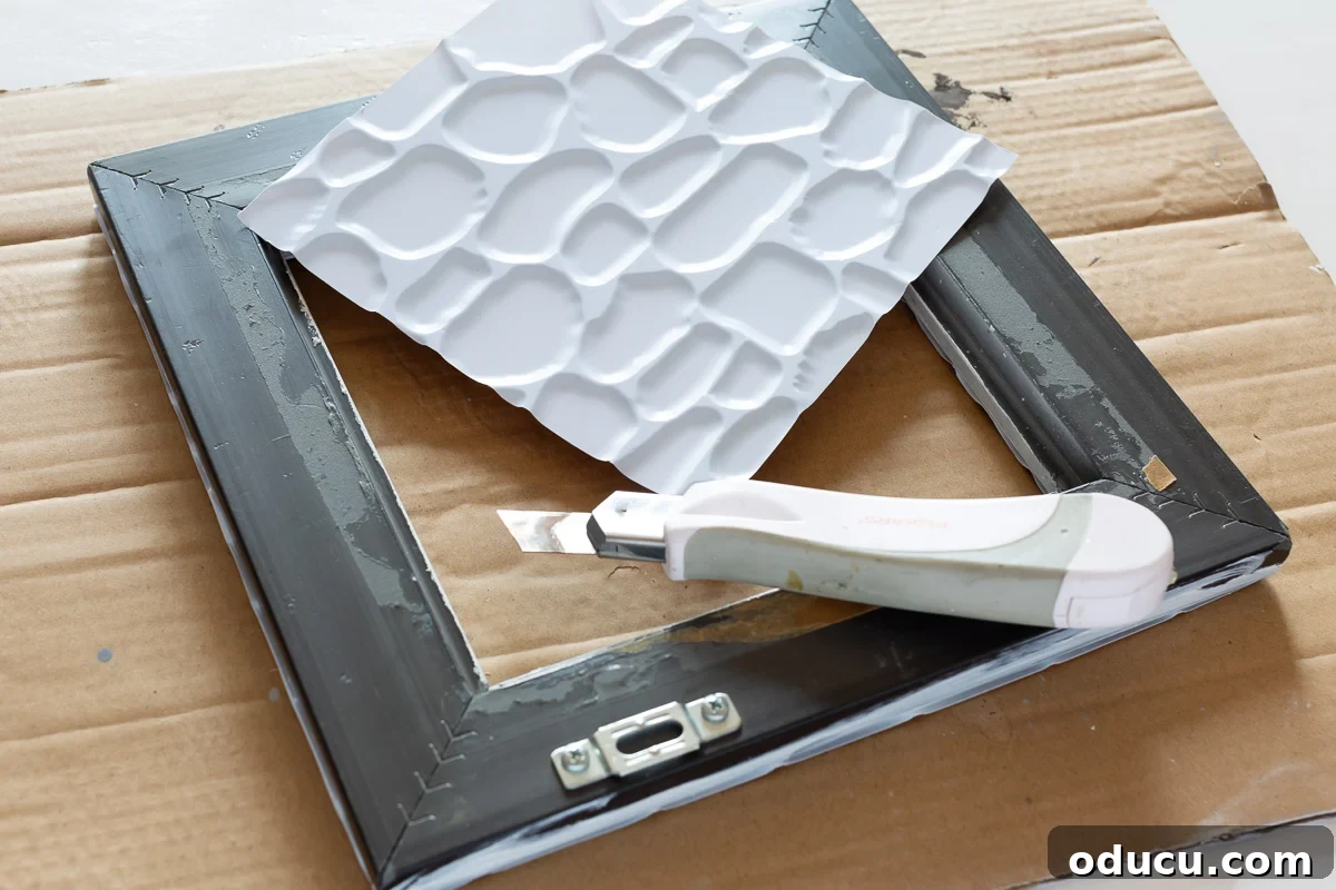 Detailed view of how to decorate a thrift store photo frame with Dollar Store adhesive tile, demonstrating precise cutting and placement.